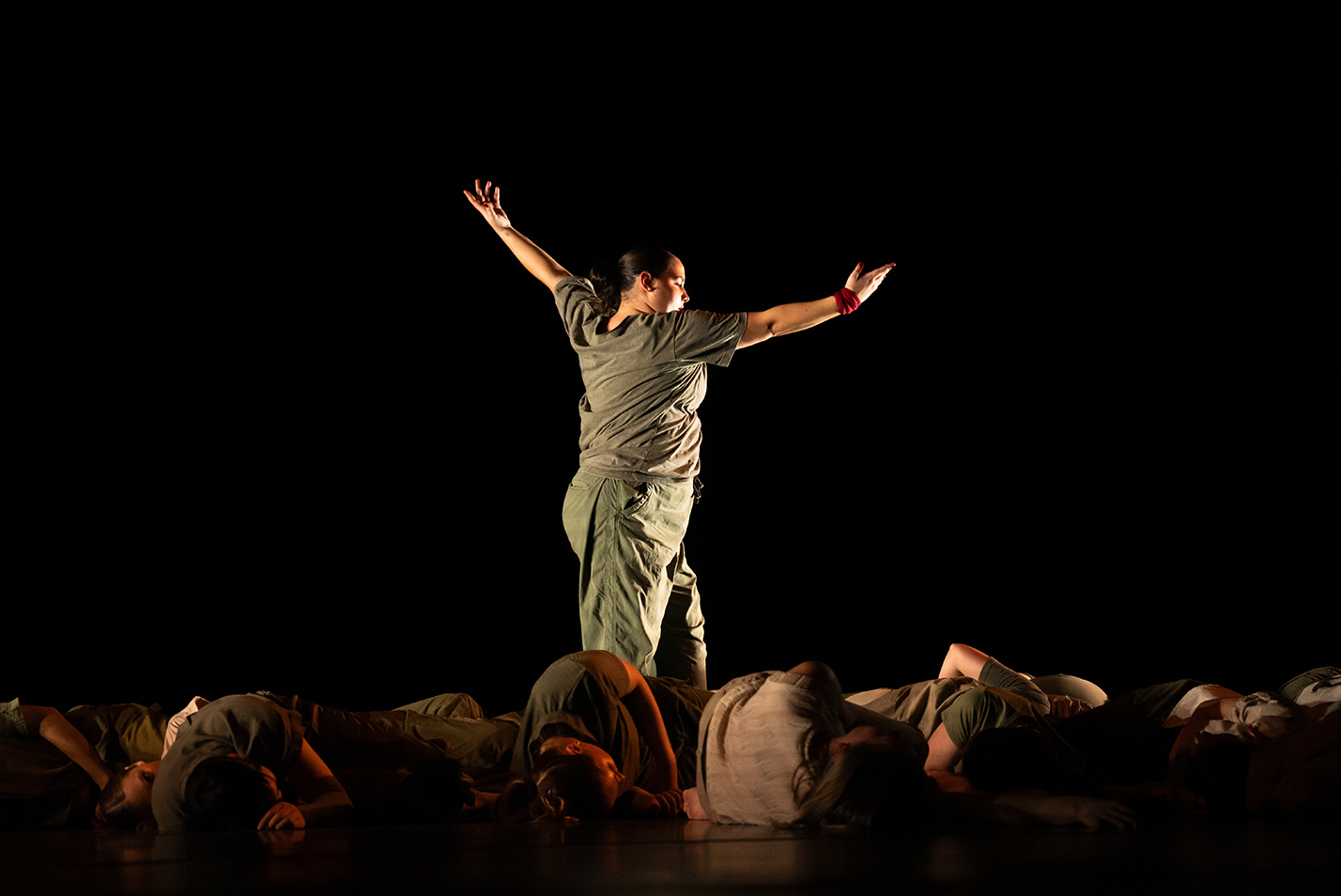 A student dancer performs on a stage with fellow dancers laying prone.