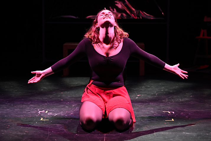 An actor bathed in red light sings out while kneeling on stage