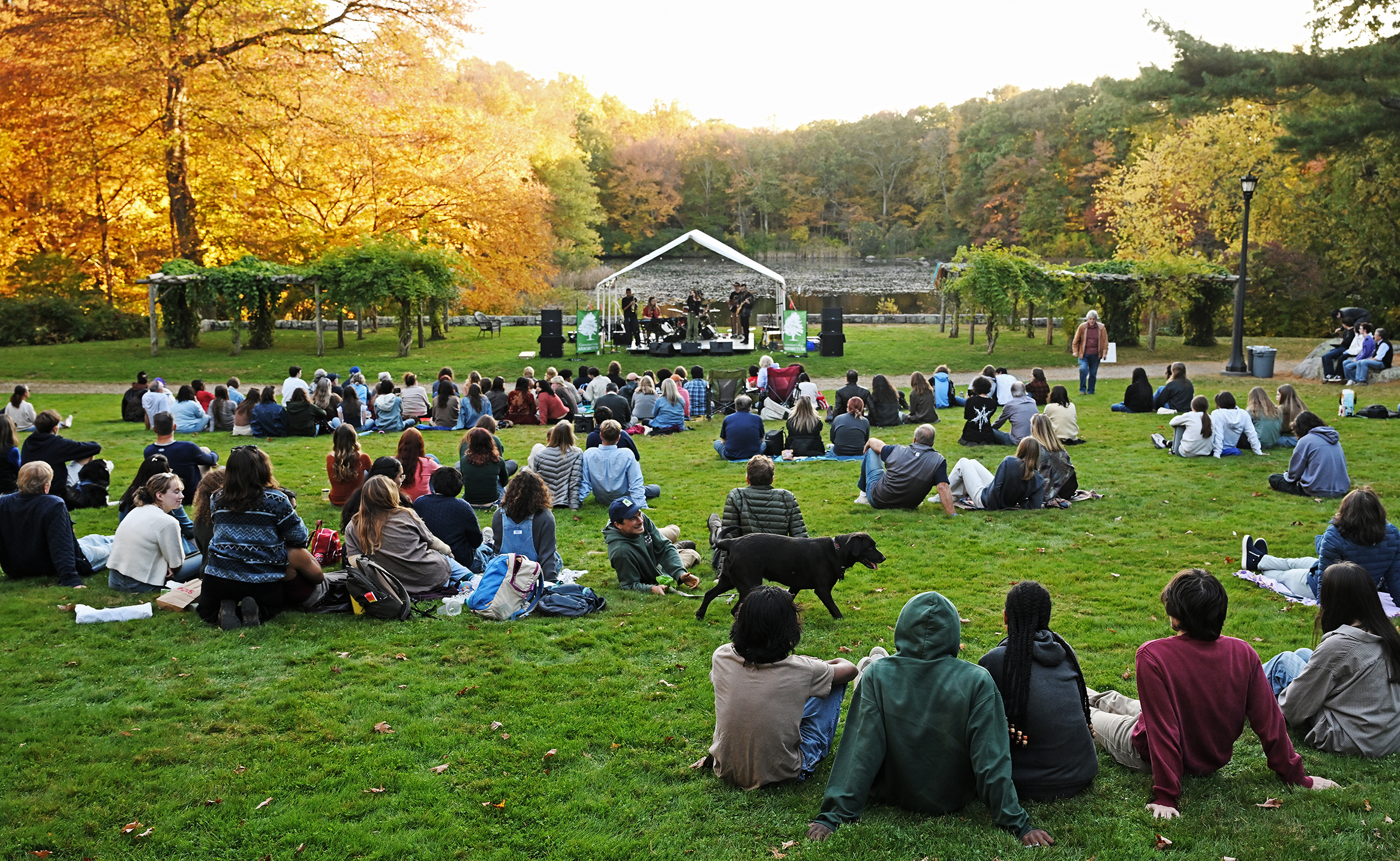 A crowd gathers on the lawn for an outdoor rock band performance on a sunny fall afternoon.