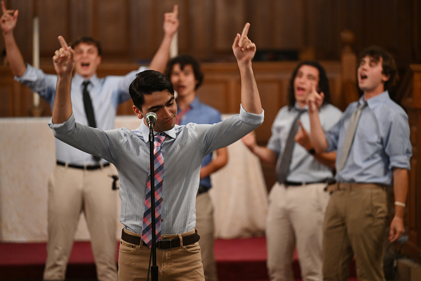 A group of singers in matching shirts and ties raise their hands during a performance