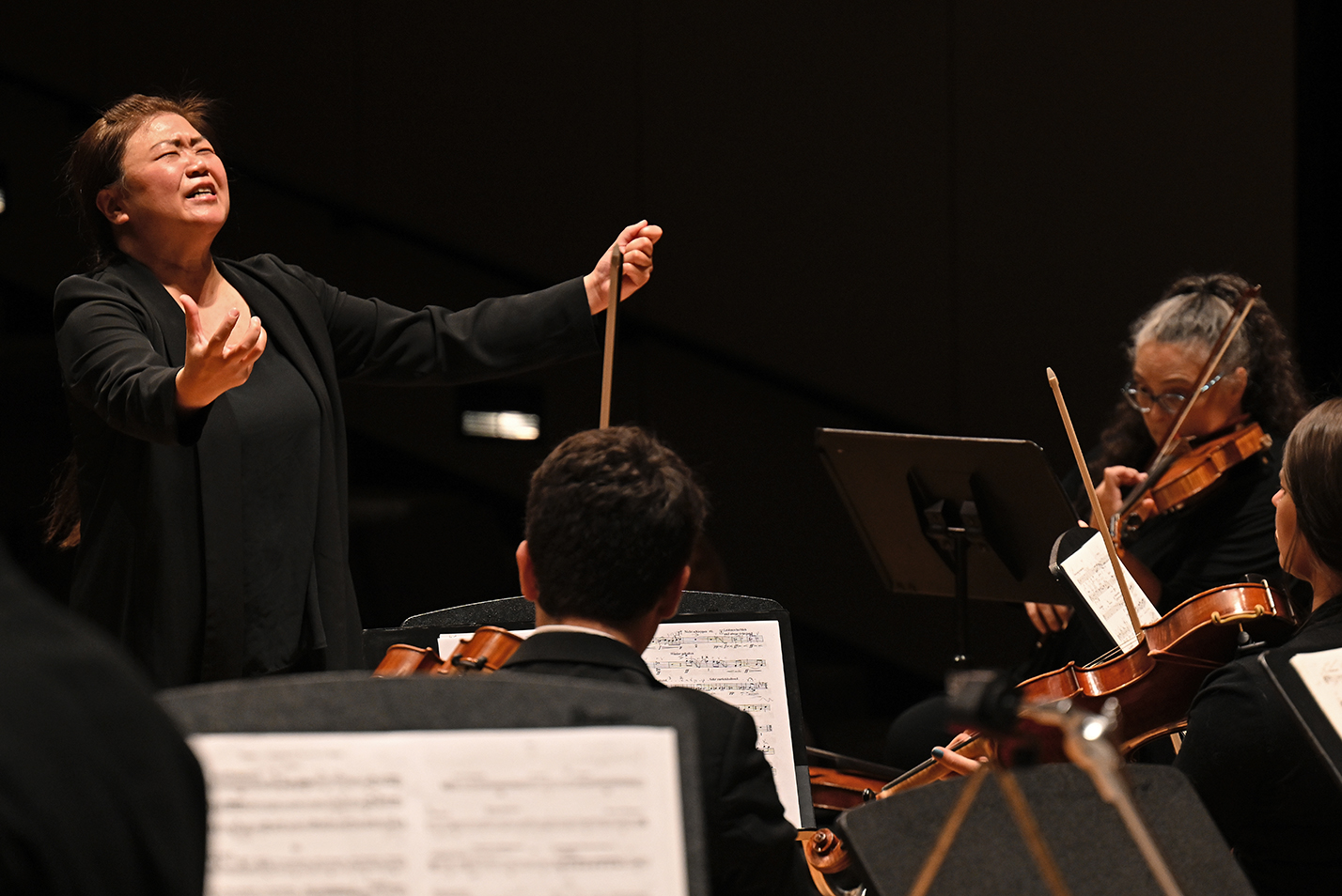 A conductor gestures as she directs a chamber orchestra